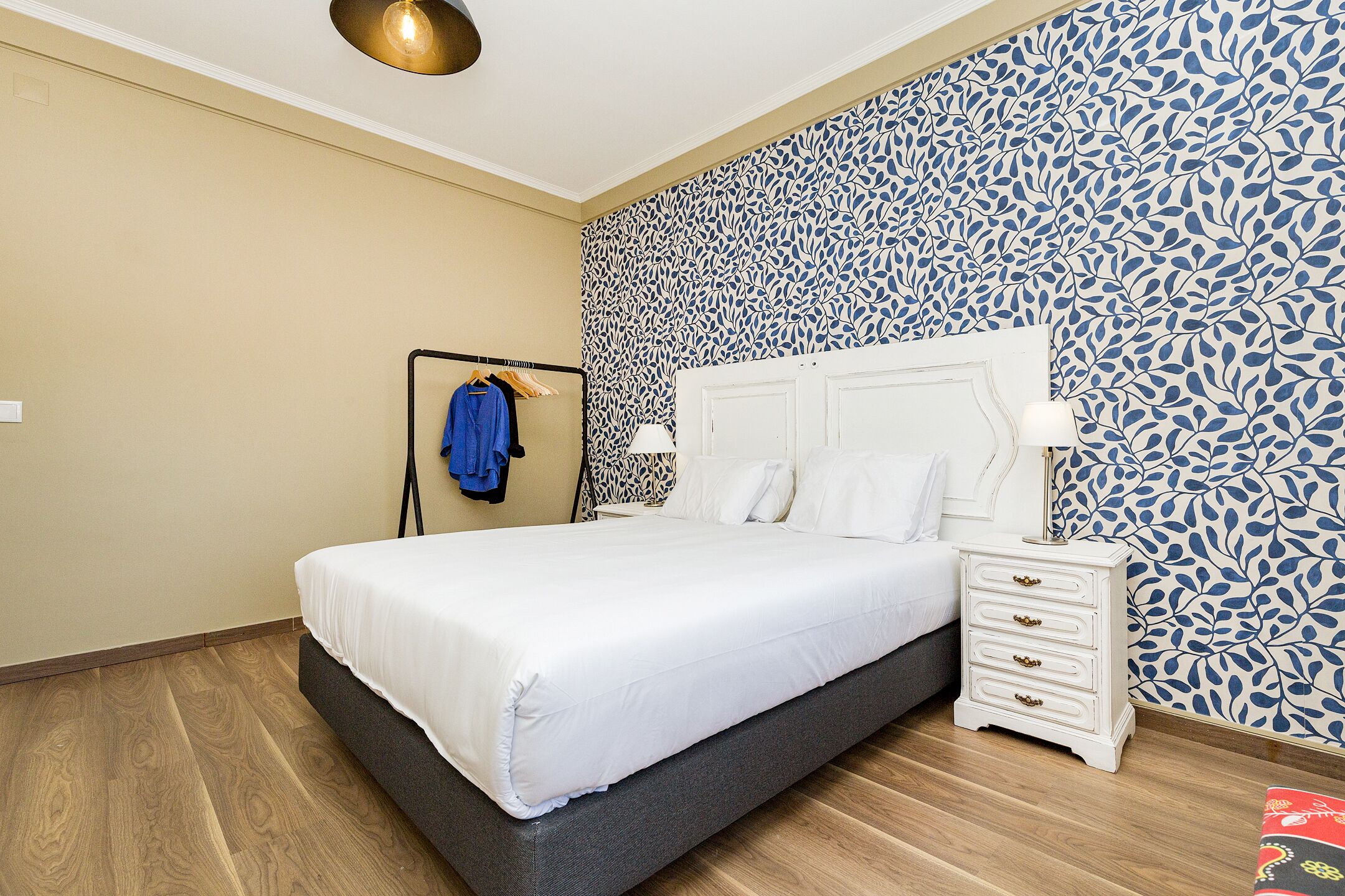 A bedroom with a bed, a nightstand, a wall with a leaf pattern, and a wooden floor.