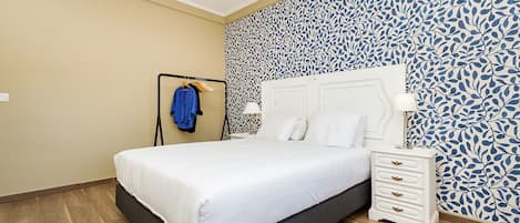 A bedroom with a bed, a nightstand, a wall with a leaf pattern, and a wooden floor.