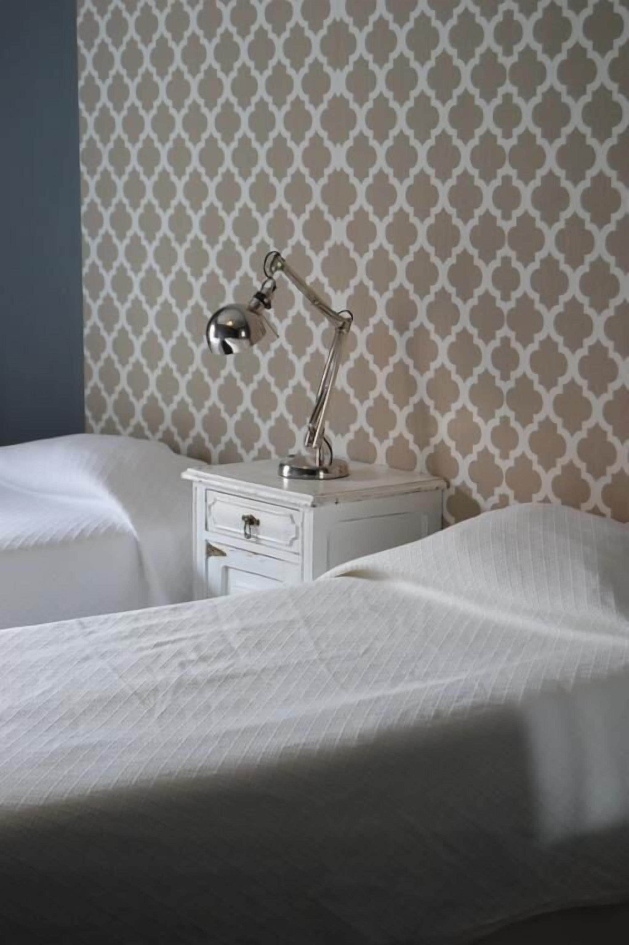 A neatly made bed with a white comforter and a small bedside table with a lamp.