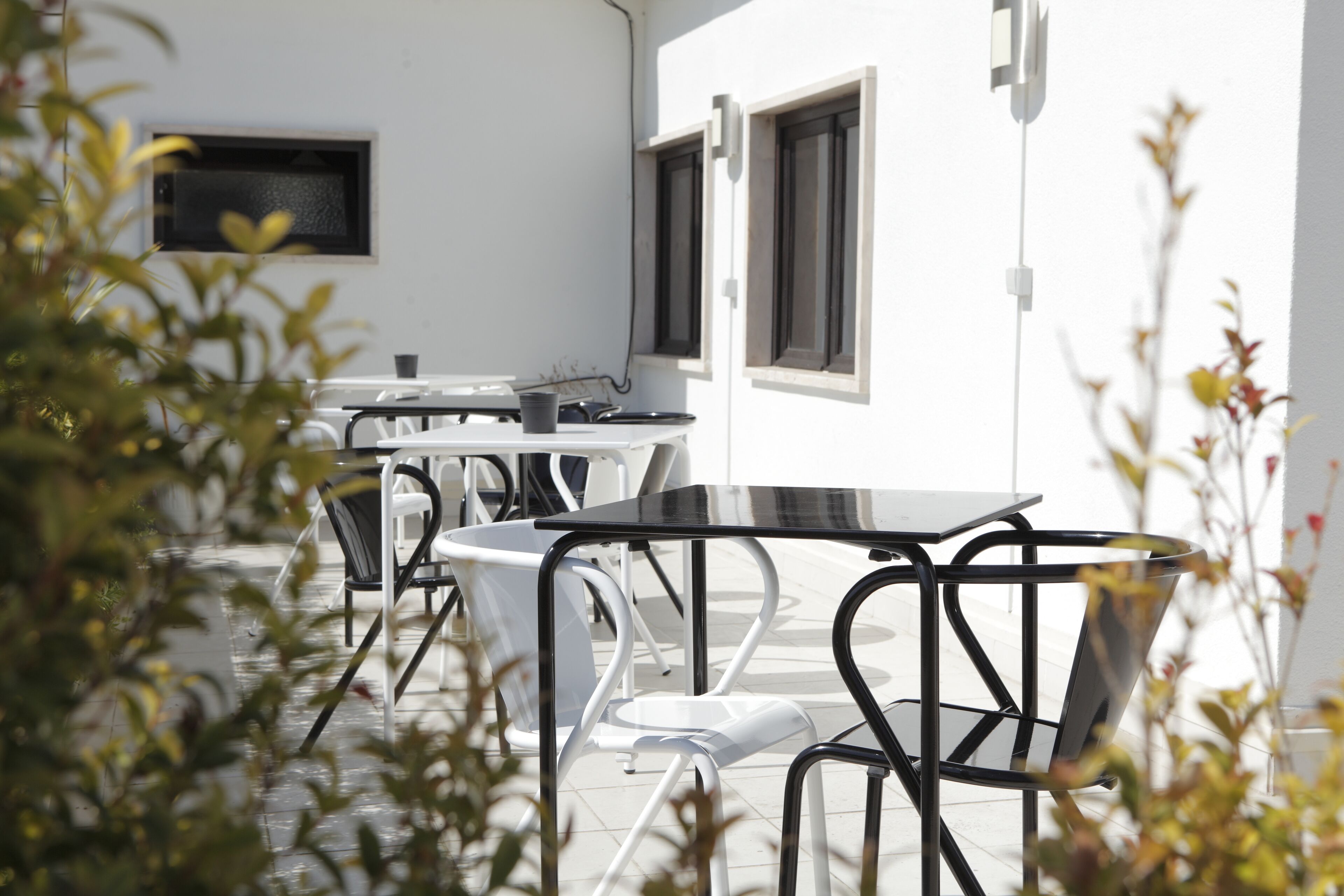 A patio area with outdoor tables and chairs, a white wall, and a window.