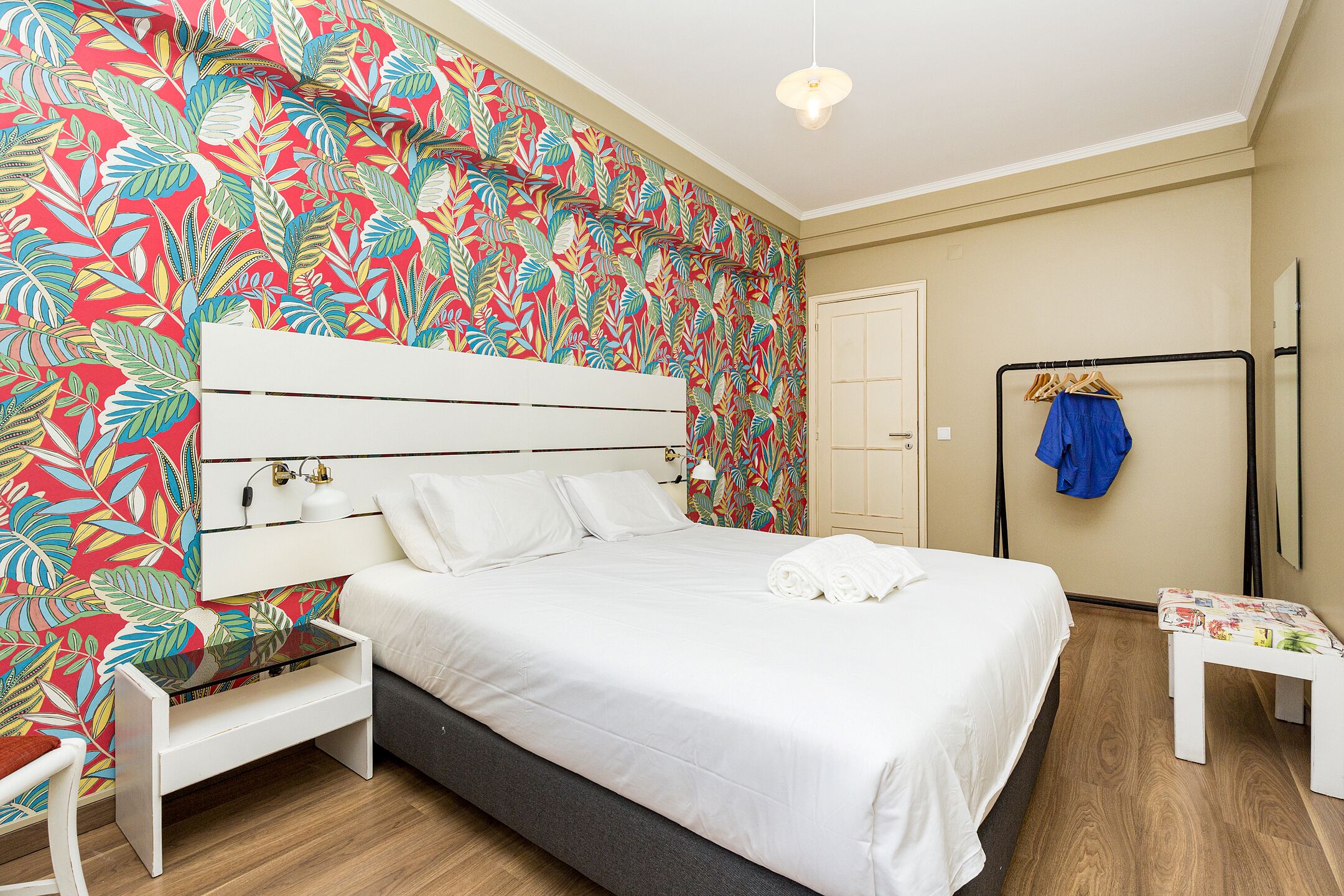 A neatly made bed with white linens, a bedside table, and a bench with a floral cushion.
