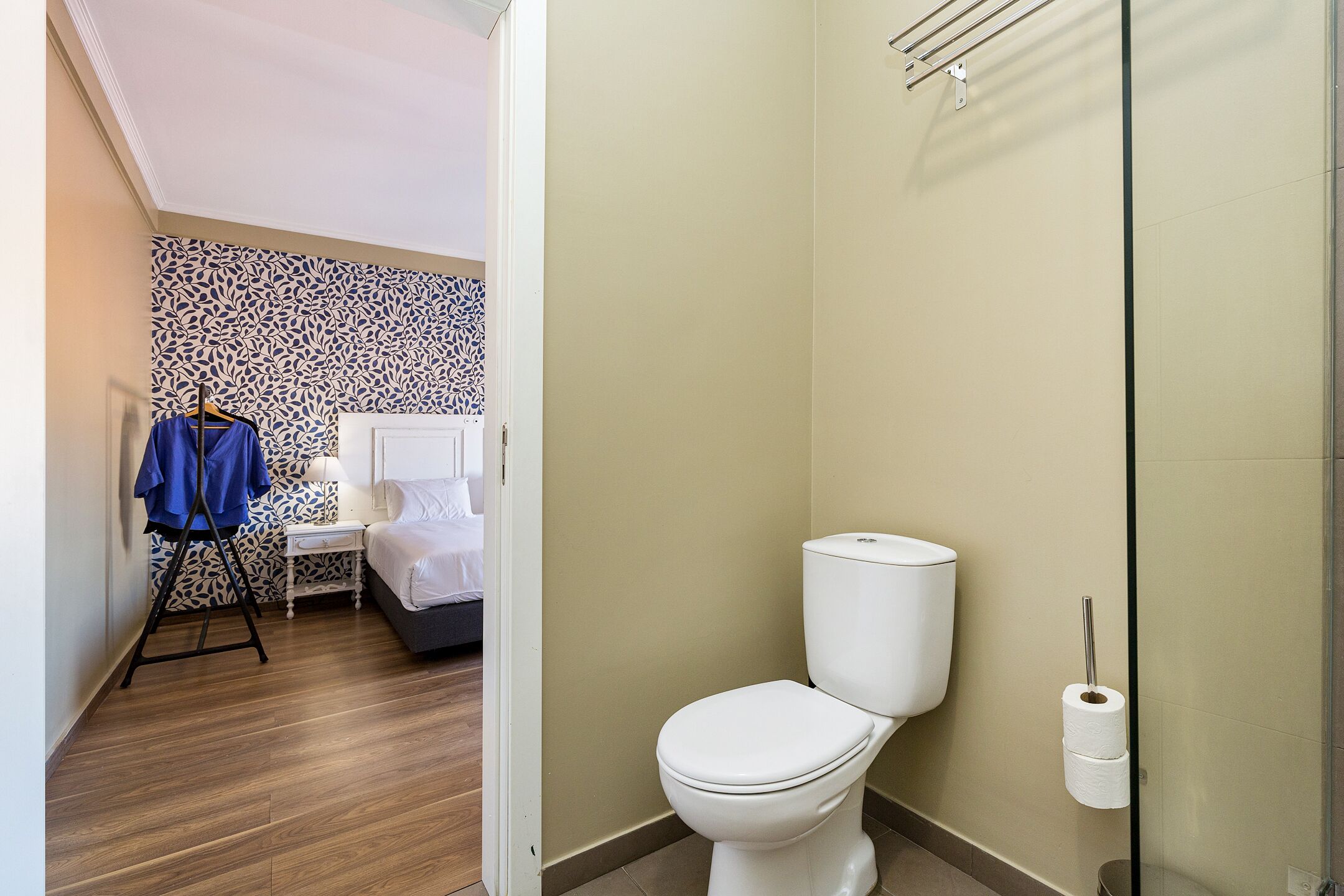 Un bagno con il water, un portasciugamani e un letto sullo sfondo.