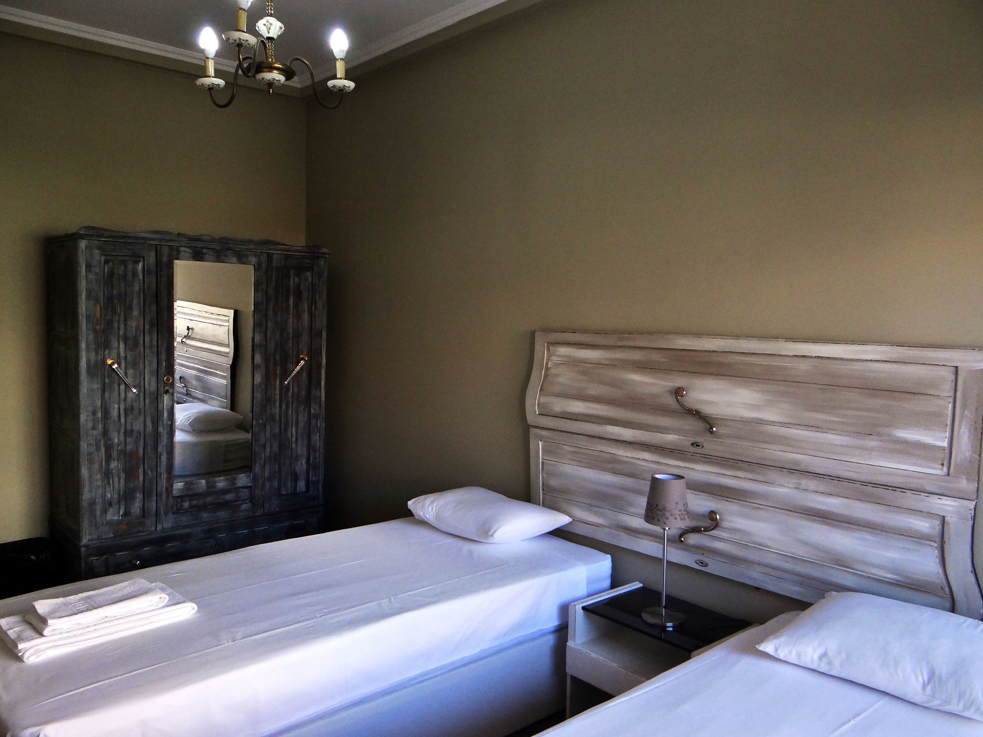 A bedroom with two beds, a wardrobe, a nightstand, and a chandelier.