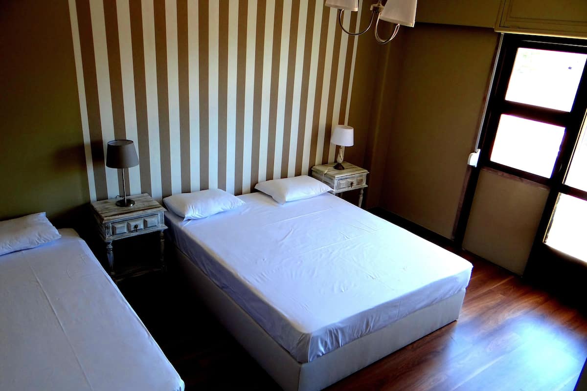 Una habitación de hotel con dos camas individuales, una mesita de noche con lámpara, un aparador y una ventana con persianas.