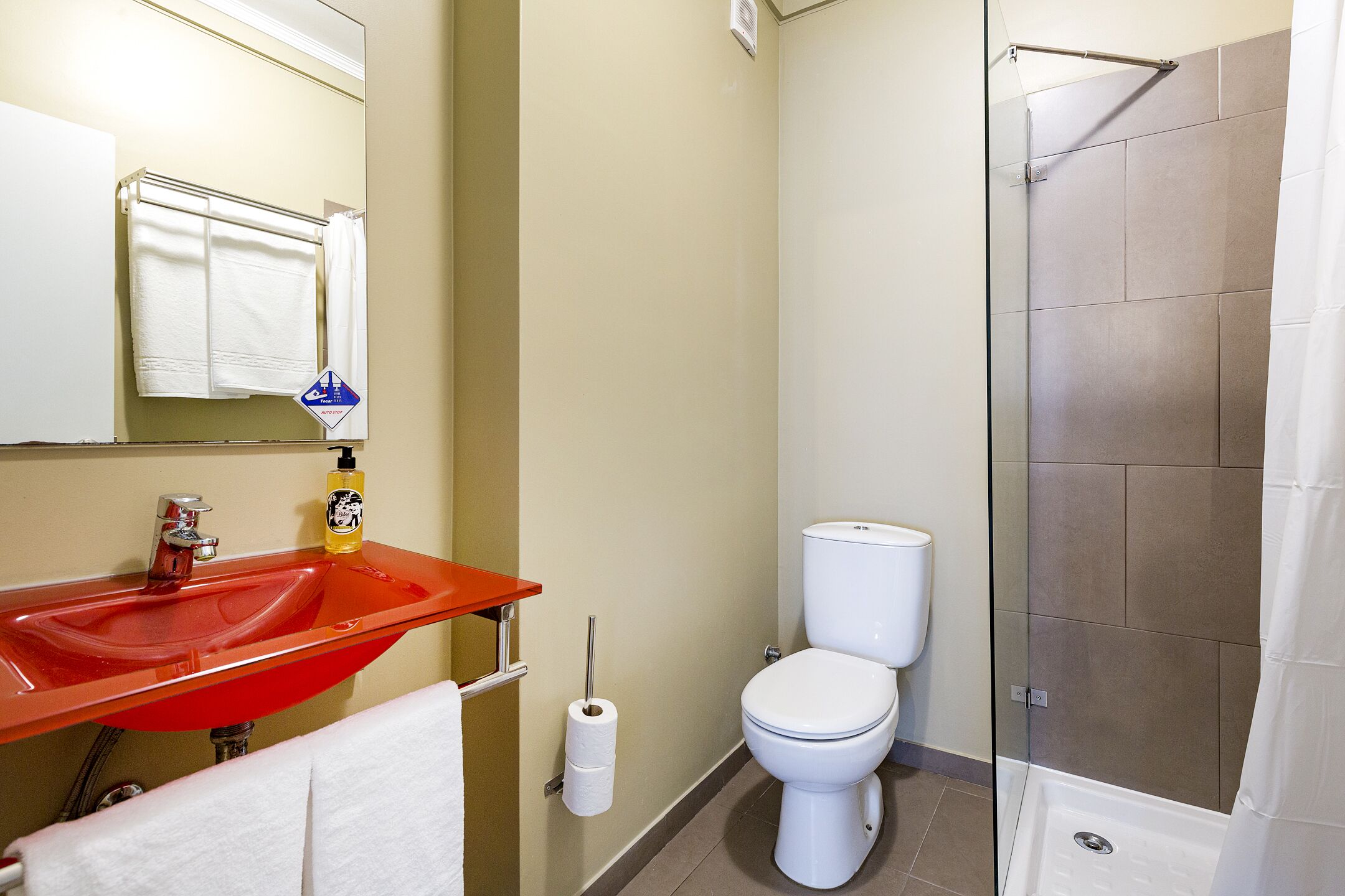 A bathroom with a red sink, white toilet, and glass shower enclosure.