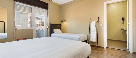 Un dormitorio con una cama grande, una mesita de noche, una lámpara, una ventana con persianas y una puerta que da a un baño.