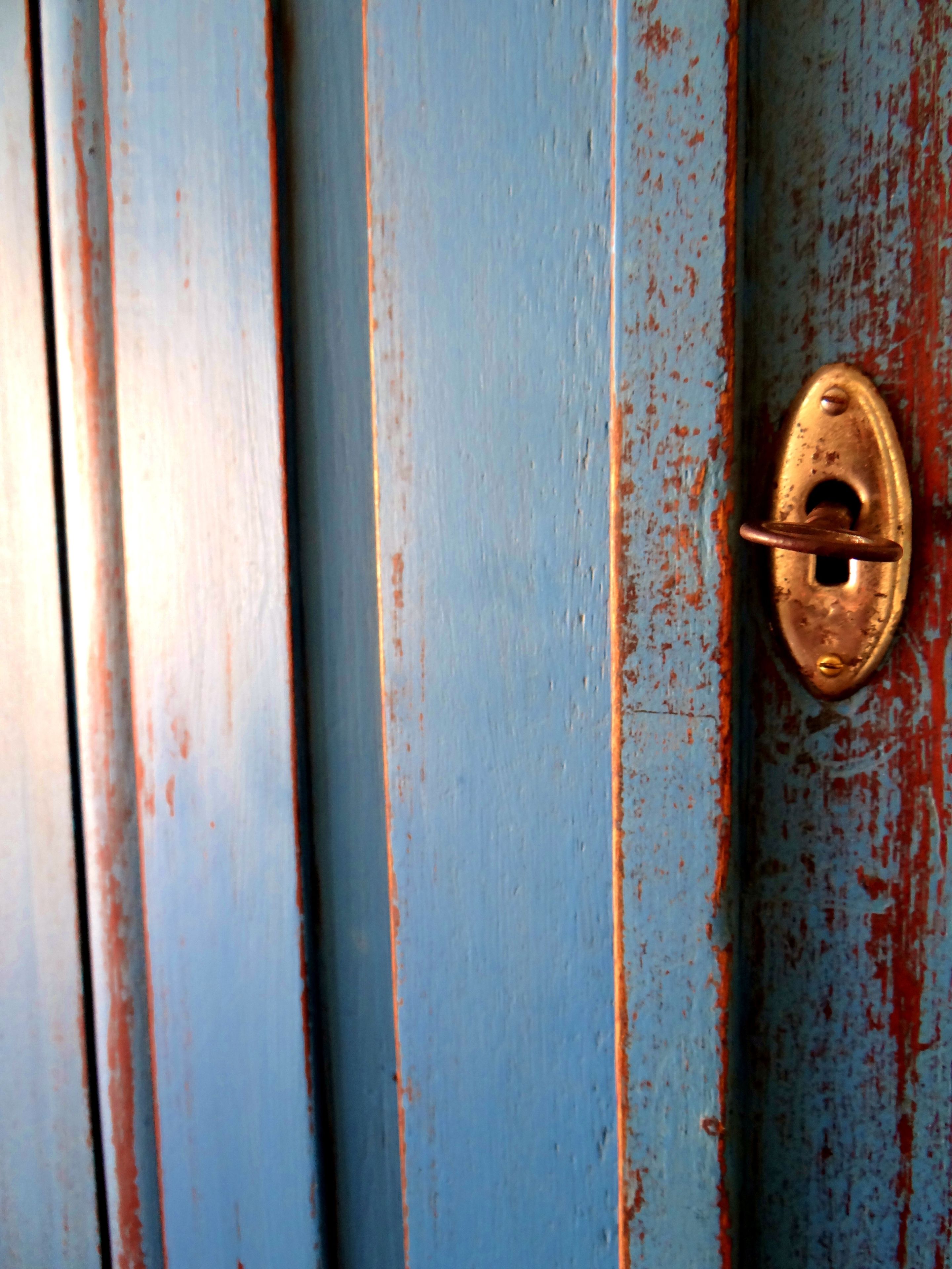 Primer plano de una puerta azul desgastada, con pintura descascarada y un picaporte de latón.