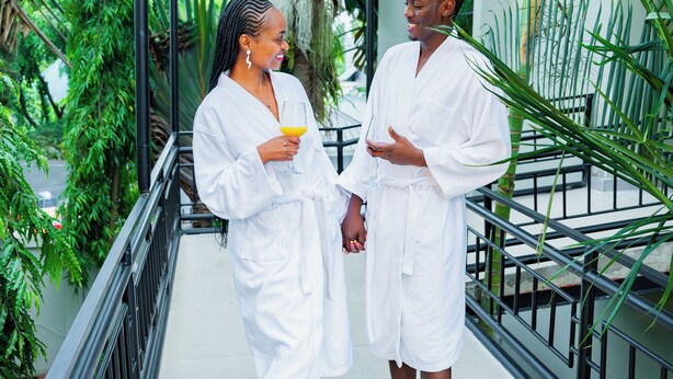 Two people in white robes on a balcony with a metal railing, surrounded by greenery. - Green Mountain Hotel (Arusha)