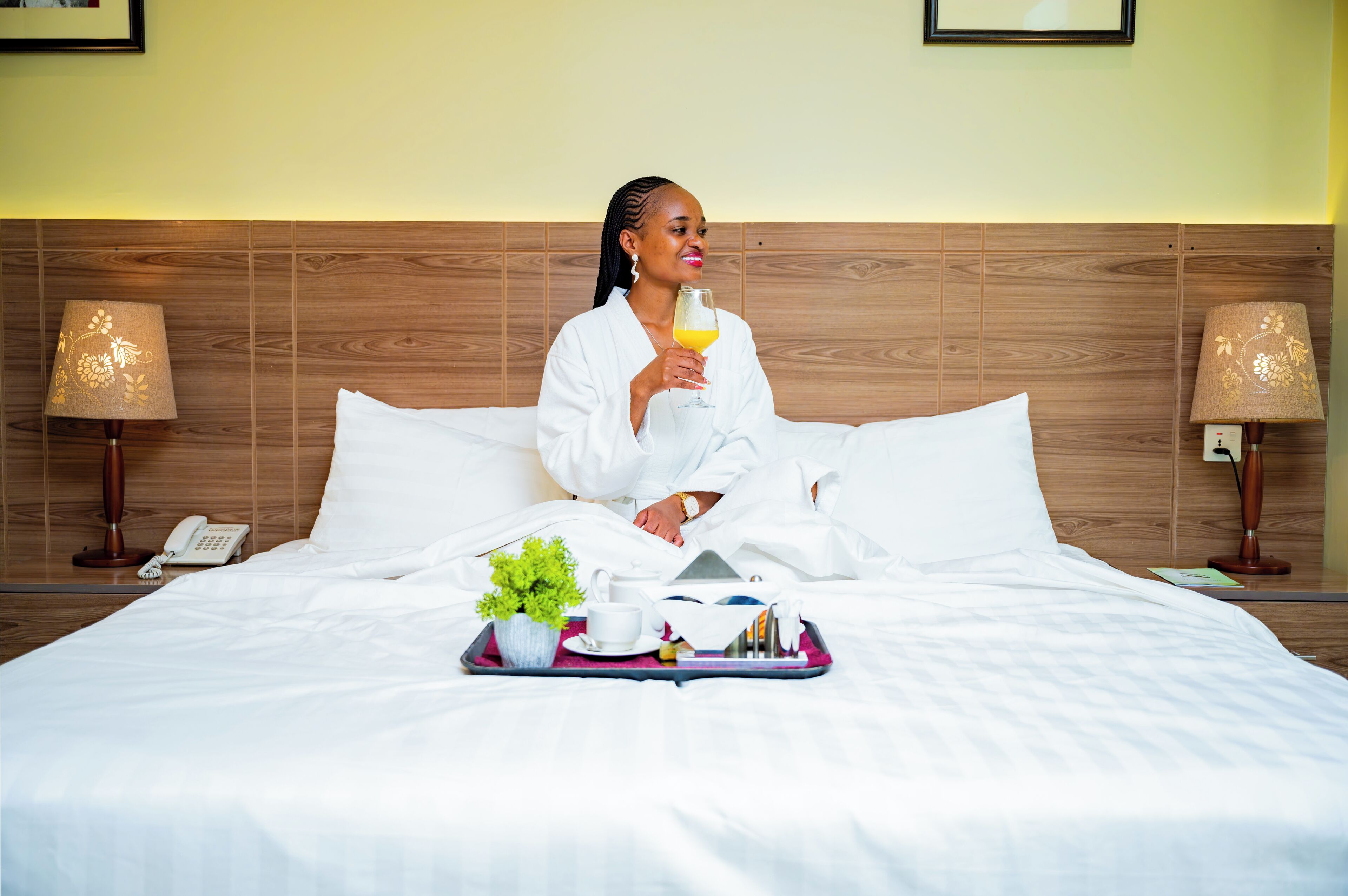 A hotel room with a bed, a tray with breakfast items, a bedside lamp, and a telephone.
