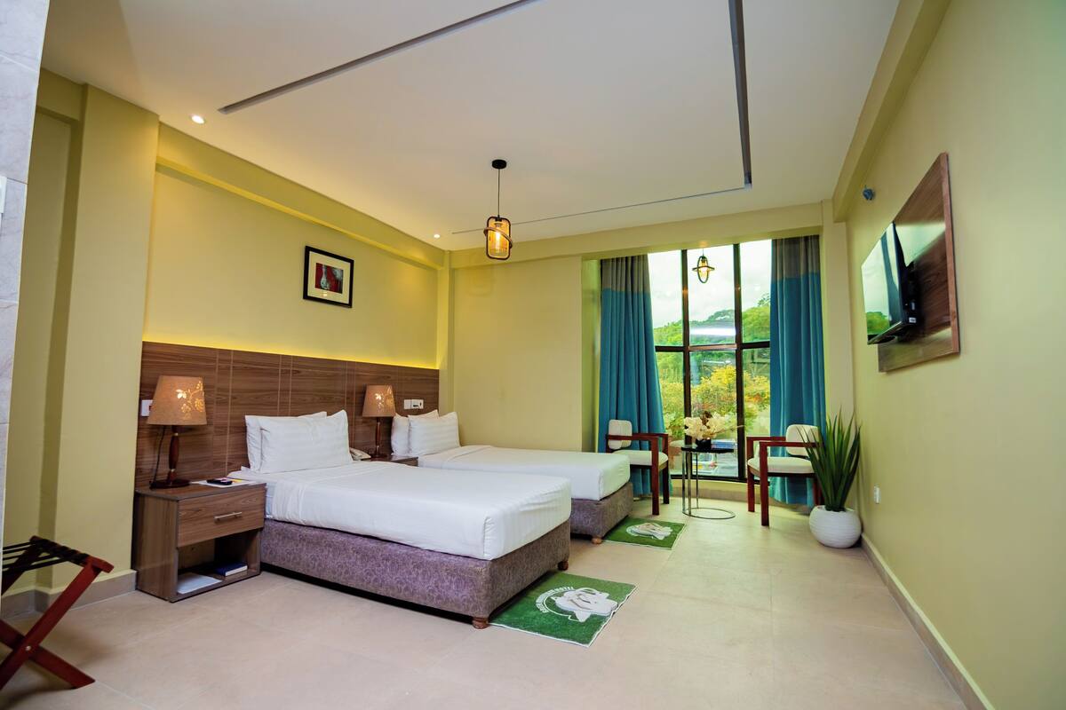 A hotel room with two beds, a TV, a desk with a chair, and a window with curtains.