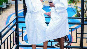 Two people in white robes by a pool with a building in the background. - Green Mountain Hotel (Arusha)