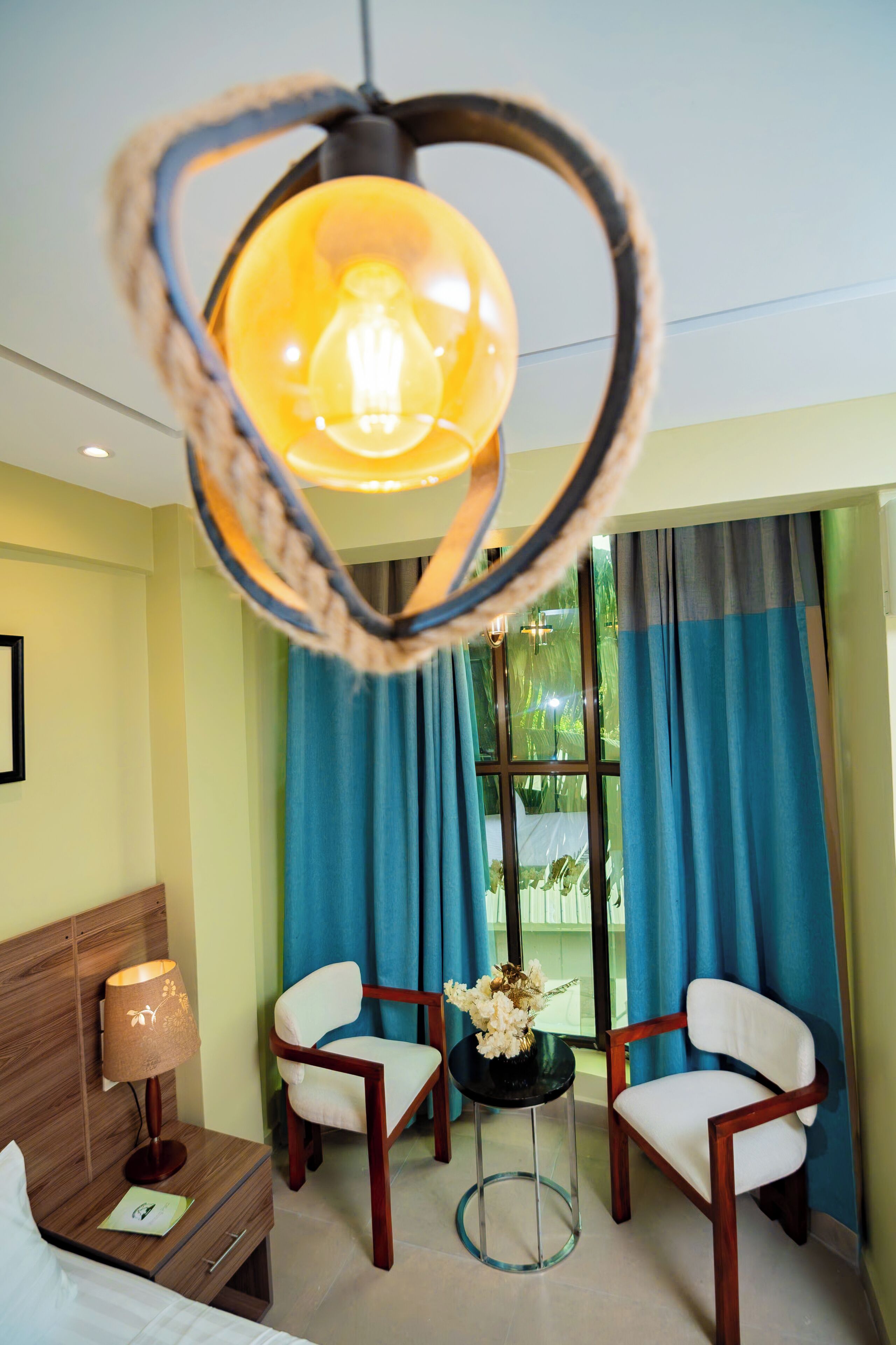 A hotel room with a bed, two chairs, a small table with a lamp, and a heart-shaped light fixture.