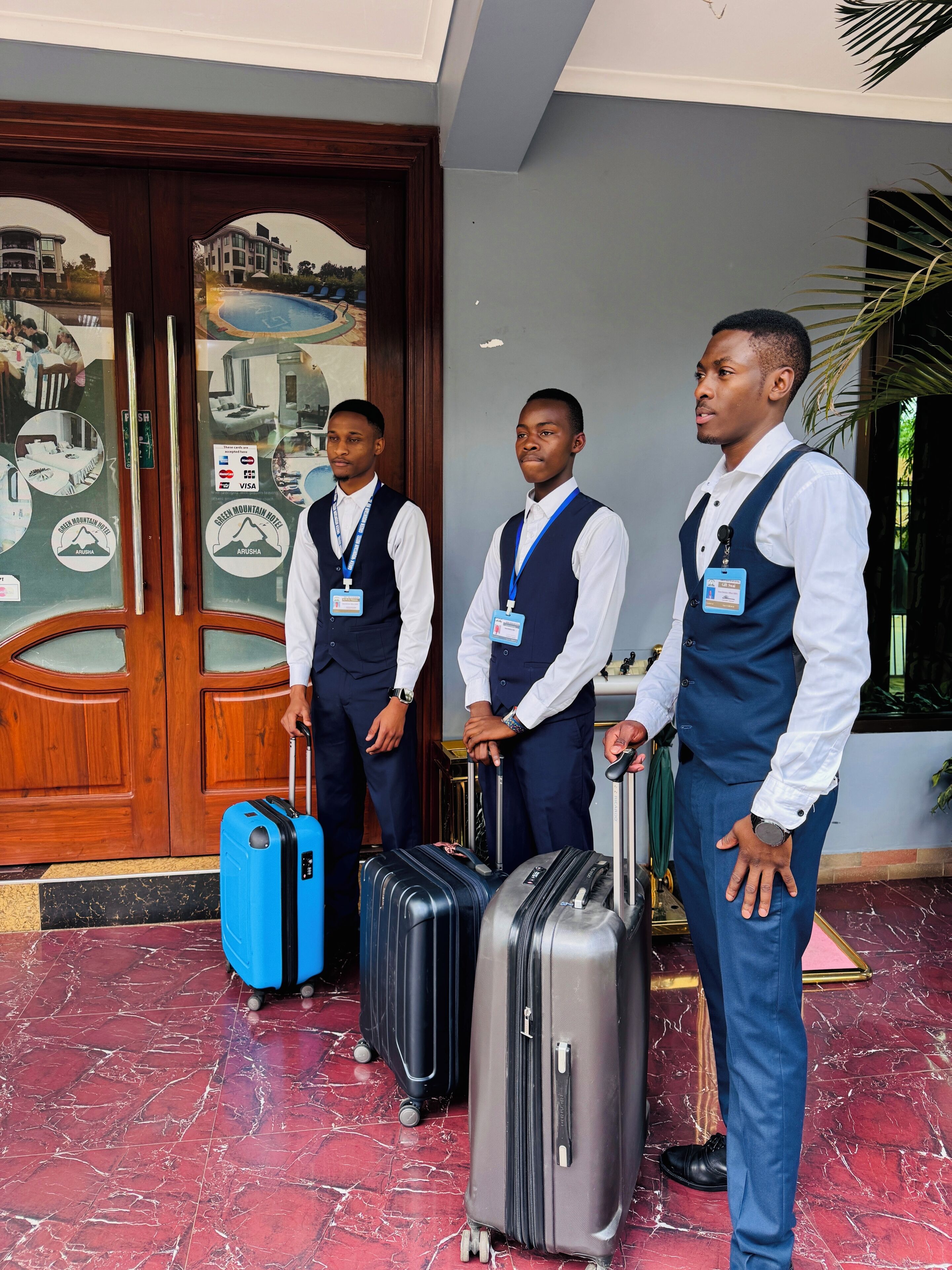 Three men in business attire standing in front of a hotel entrance with a wooden door and a mural. They are holding suitcases.