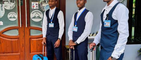 Three men in business attire standing in front of a hotel entrance with a wooden door and a mural. They are holding suitcases.