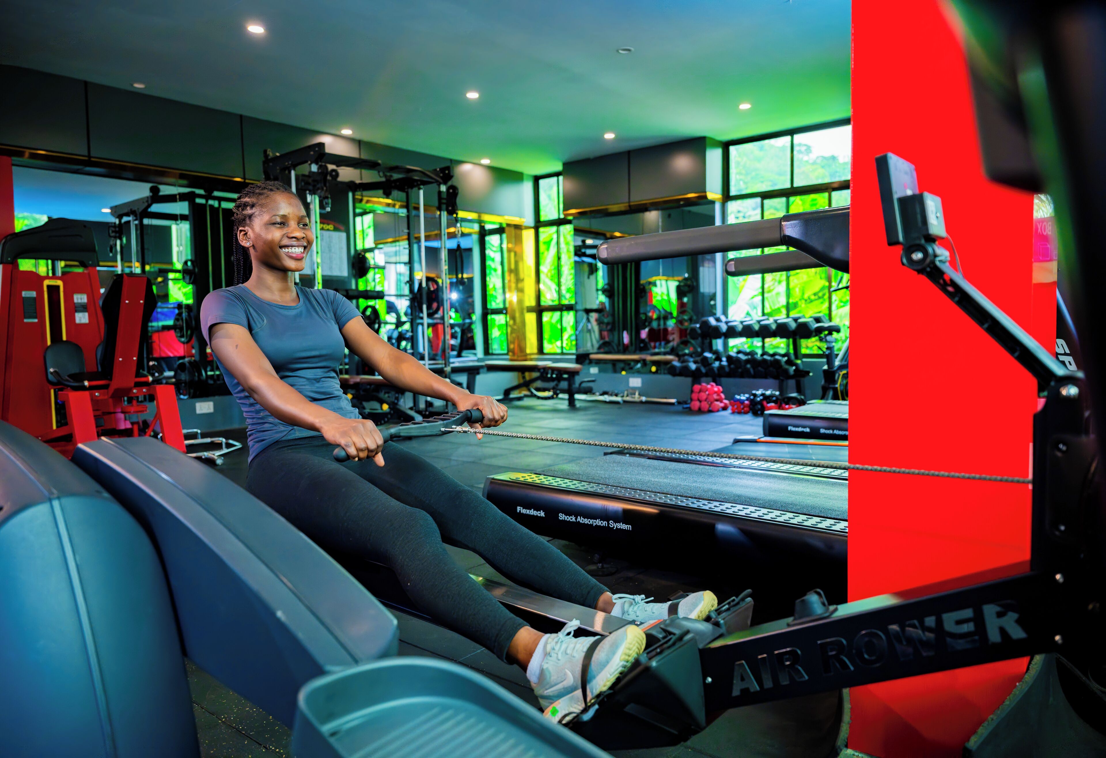 Et fitnesscenter med romaskiner, vægttræningsudstyr og udsigt til grøn vegetation udenfor.