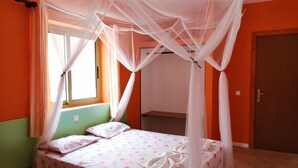 A bedroom with a bed under a canopy, a window with curtains, and an orange wall.