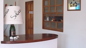 A reception desk with a lamp, a wooden door, a window with a view of the outside, and a framed picture on the wall.