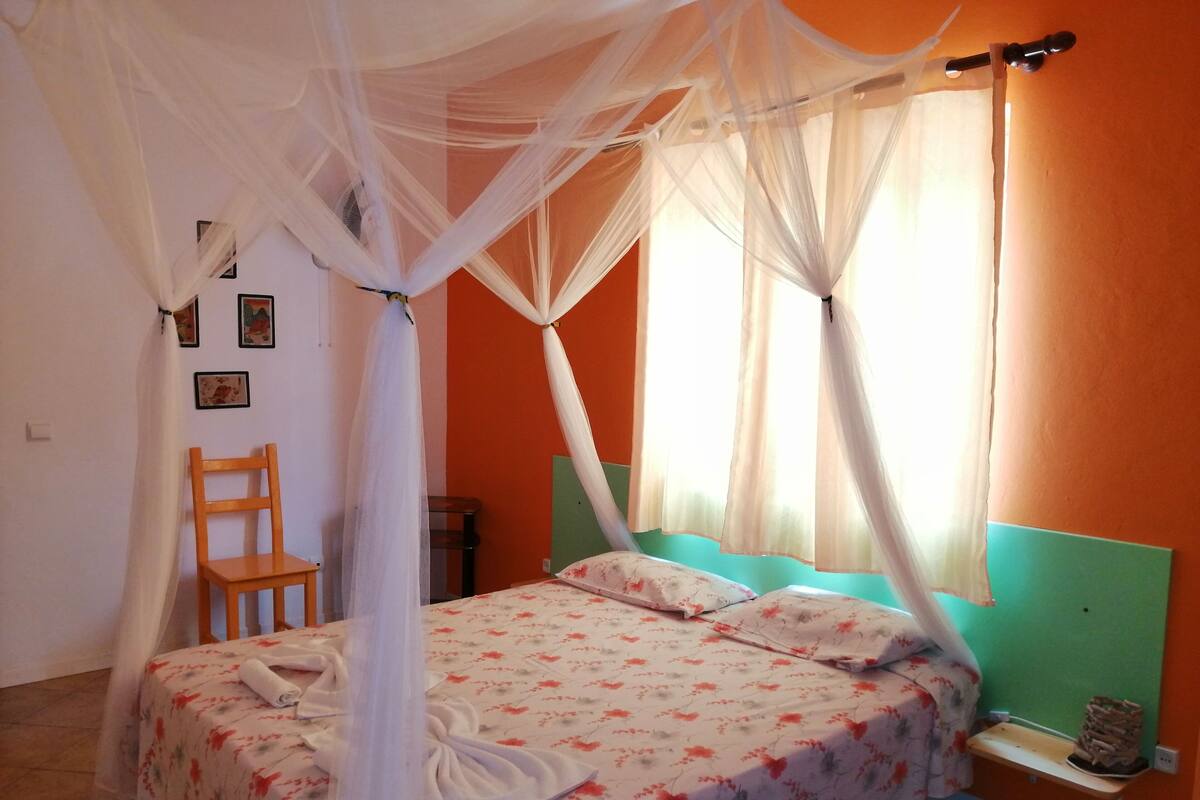 Un dormitorio con cama, una silla, una mesita de noche y una ventana con cortinas.