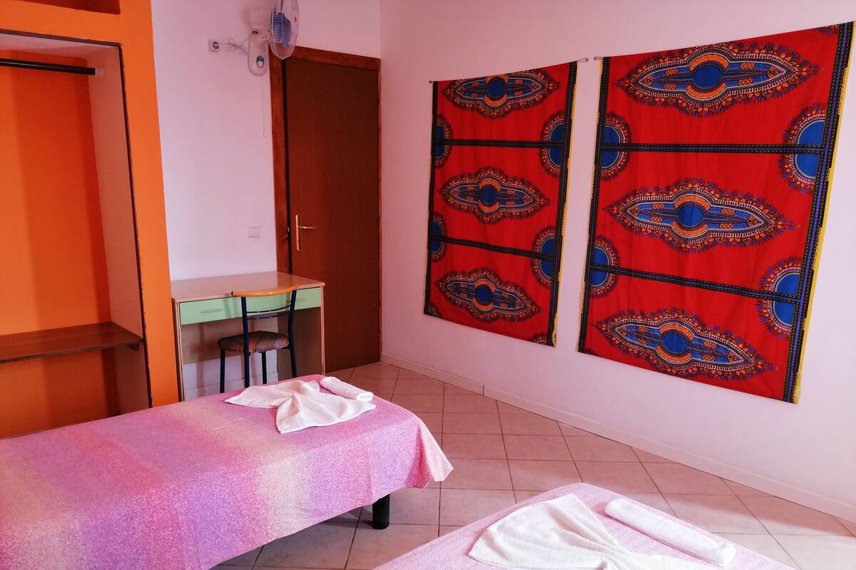 Una habitación con dos camas, un escritorio y una pared con cortinas estampadas.