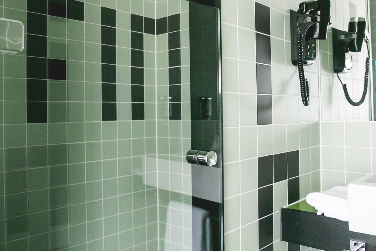 A bathroom with green and black tiles, a glass shower enclosure, a towel rack, and a mounted telephone.