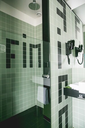 A bathroom with green and black tiles, a glass shower enclosure, a towel rack, and a mounted telephone.