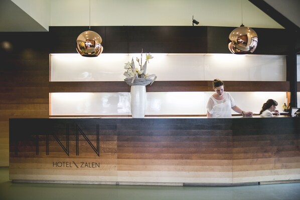 A hotel reception desk with a wooden panel design and a large vase of flowers.