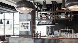 A bar area with a rustic wooden counter, multiple stools, hanging lights, and a variety of bottles and glasses.