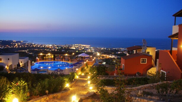 Un resort con piscina, vista sul mare e un vialetto ben illuminato che conduce alla piscina.