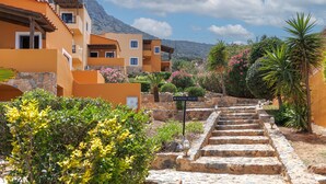 Una scalinata in pietra conduce a un edificio con numerosi balconi, immerso nel verde e sullo sfondo montagne.