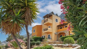 Un edificio a più piani con balconi, immerso nel verde e circondato da fiori rosa.