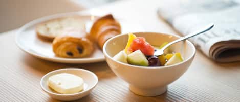 Una escena de desayuno con un bol de fruta, un croissant y mantequilla sobre una mesa.