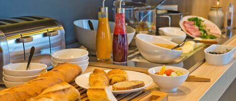 A breakfast buffet with bread, croissants, fruit, and various condiments.