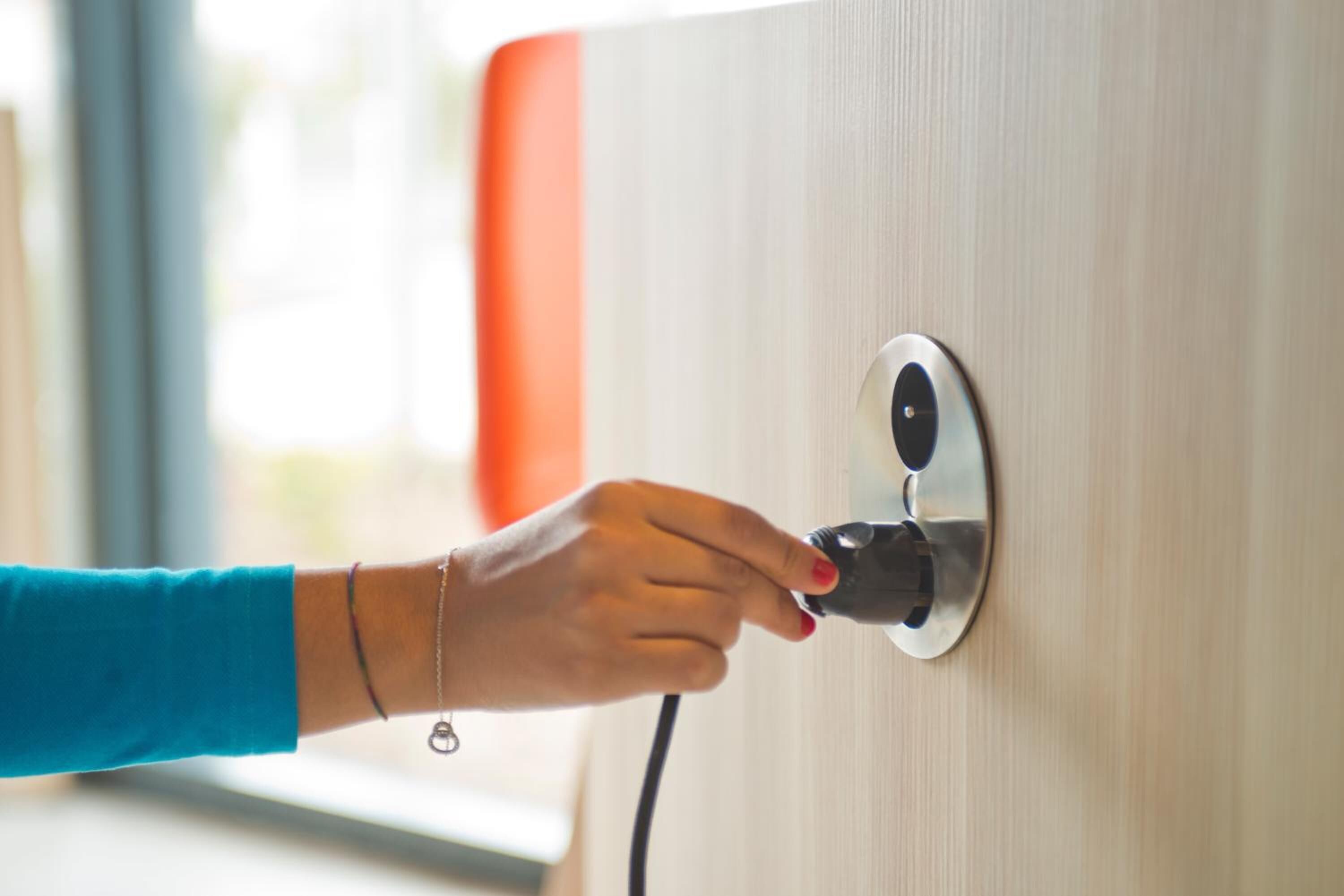 A hand plugging a device into a wall socket.