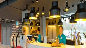 Zona de bar moderna con lámparas colgantes negras, sillas rojas y una barra donde el personal atiende.