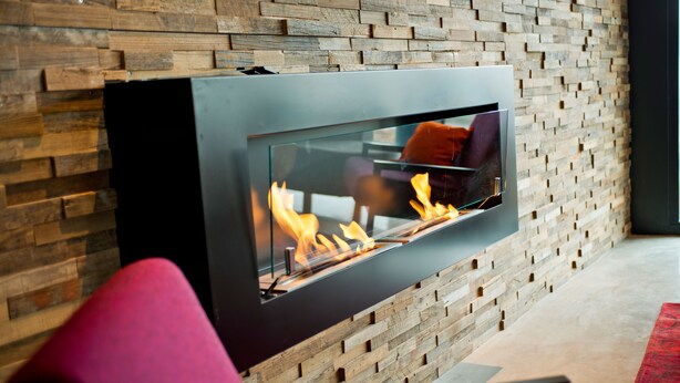 Una chimenea moderna con frente de vidrio, ubicada frente a una pared de madera.