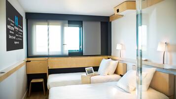 A hotel room with two beds, a small desk, a laptop, and a window with curtains.