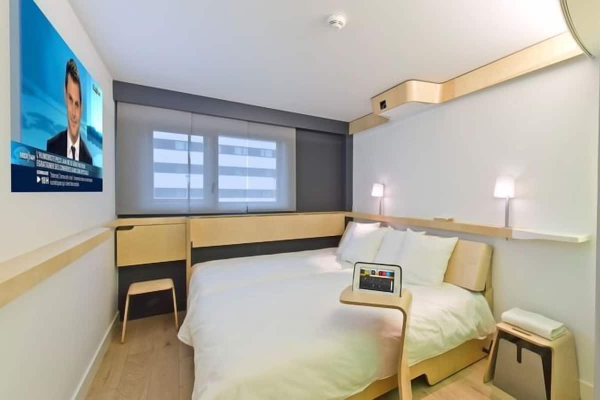 Een hotelkamer met een bed, nachtkastje, lamp en een televisiescherm.