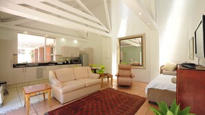 A spacious living area with a sofa, a dining table, a chair, and a bed. There is a kitchen in the background with cabinets and a window. - Fifteen On Orange (Johannesburg)