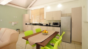 A compact kitchen with a dining area, featuring a wooden table, green chairs, and a bowl of fruit. - Fifteen On Orange (Johannesburg)