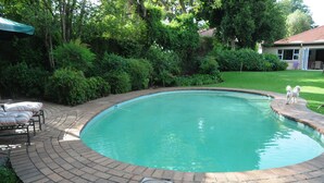 A circular swimming pool with a brick border, surrounded by lush greenery and a patio area with outdoor furniture. - Fifteen On Orange (Johannesburg)