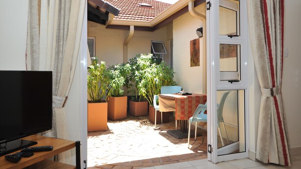 A sunlit patio with a TV, seating, and potted plants. - Fifteen On Orange (Johannesburg)