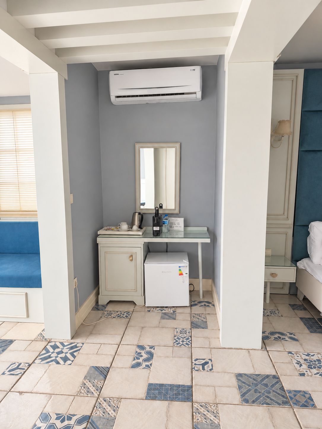 A room with a kitchenette, a mirror, a bed, and a patterned floor.