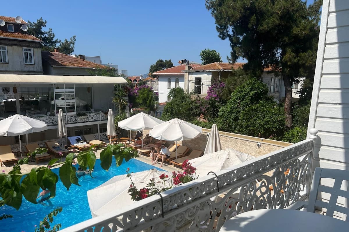 A pool area with lounge chairs and umbrellas, surrounded by buildings and greenery.
