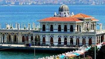 Un edificio histórico con cúpula y ventanas de arco, situado cerca de una costa con un paisaje urbano al fondo.