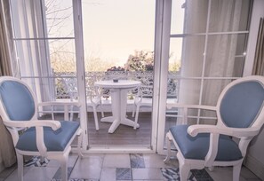 A balcony with two white chairs with blue cushions, a small round table, and a view of trees and buildings in the background. - Buyukada Cankaya Hotel (Adalar)