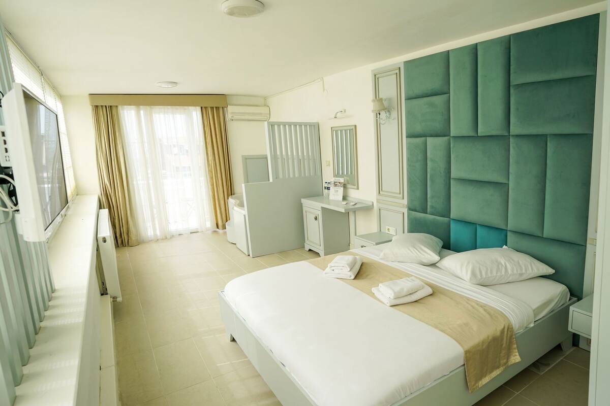 A hotel room with a bed, a desk, a chair, a TV, and a window with curtains.