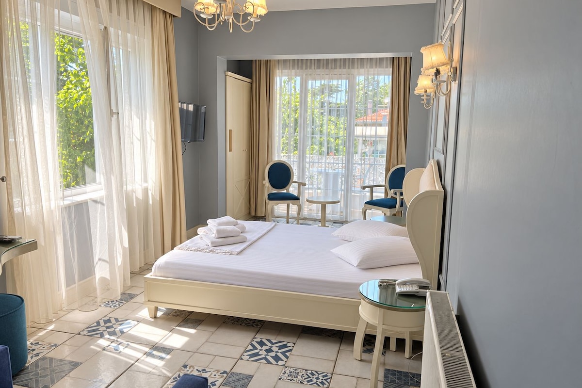 A hotel room with a bed, two chairs, a small table, a TV, and a view of the outdoors.