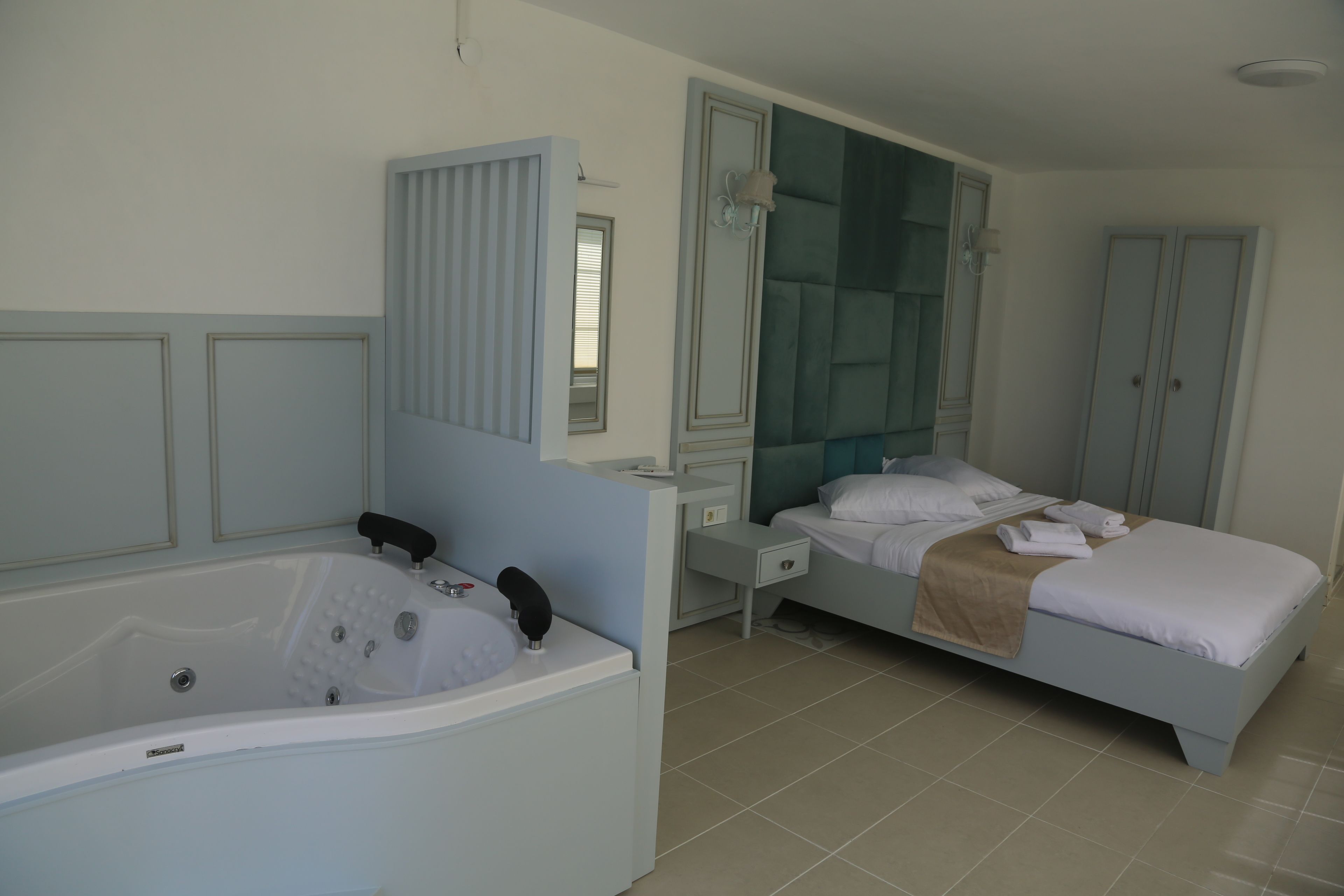 Une chambre à coucher avec une grande baignoire, un lit avec une literie blanche, une table de chevet et une armoire.