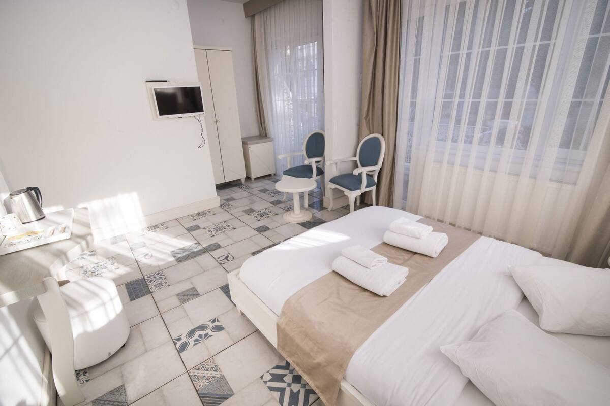 A hotel room with a bed, a desk, a chair, a TV, and a window with curtains.