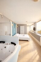 A modern hotel room with a large bathtub, two beds, a view of the sea, and a television on the windowsill.